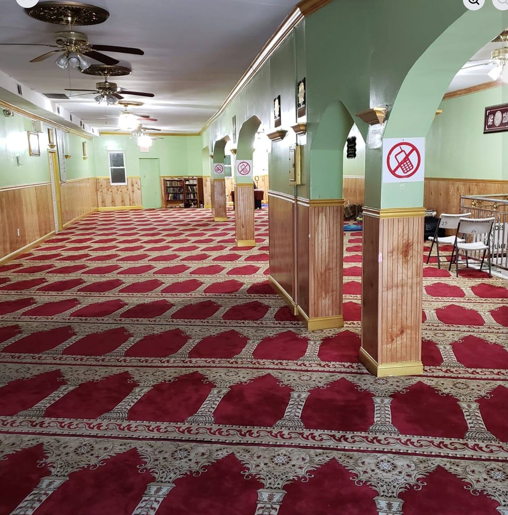 Inside the prayer hall at Masjid Fallahee — green archways, prayer carpet, and warm wood.